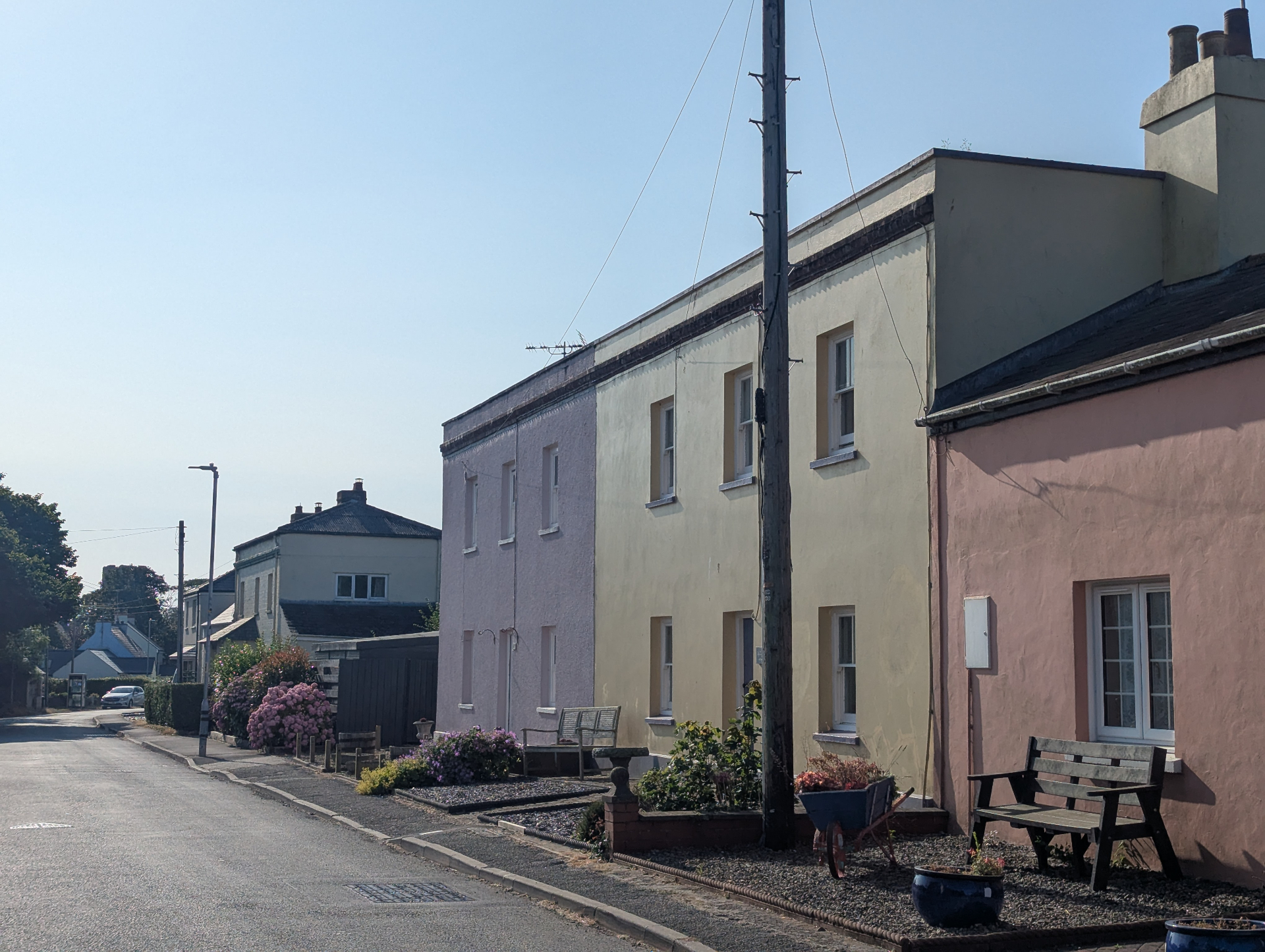 A row of pastel-painted cottages along a quiet village street in Angle, with benches and summer flowers in the foreground.