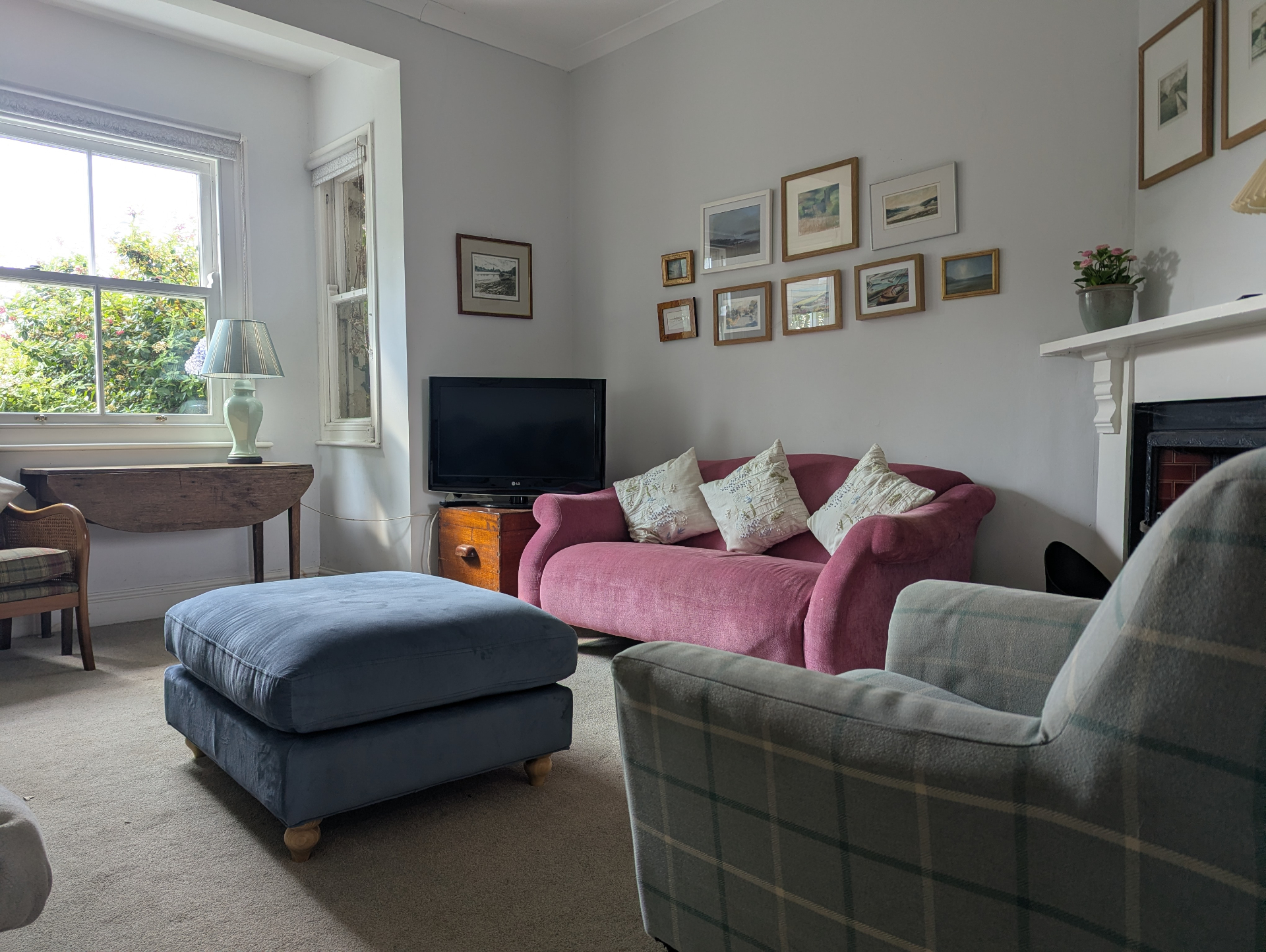 The main living room with the fireplace, pink sofa and blue footstool by the window.