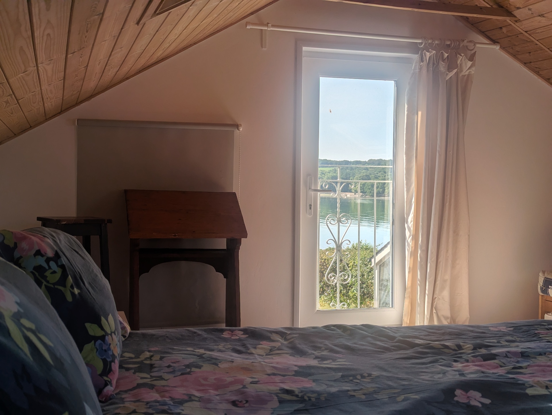The bedroom above the boathouse - pitched pine ceiling, a tall French door opening onto a small balcony above the water.